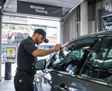 Professional applying window tint in auto shop with 'Window Tinting' text